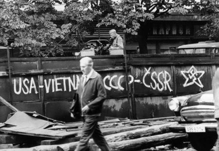 April 1968, Prague, Czechoslovakia: A Russian soldier lights a cigarette as a Czech walks past a sign which equates U.S. policy in Vietnam with the Soviet (CCCP) occupation of Czechoslovakia (CSSR). A swastika painted inside a star (which is used as a symbol for both the Soviet and the American armies) completes the barb. Since Warsaw Pact forces invaded Czechoslovakia, signs like this were scrawled on walls, windows and even Russian tanks